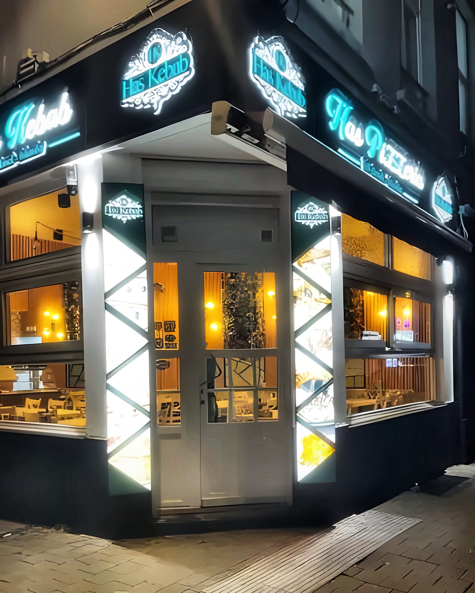 La devanture de Has Pide Kebap le soir : enseignes turquoise allumées, salle éclairée derrière les vitrines